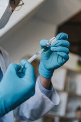 Doctor wearing protective glove preparing COVID-19 dose syringe while at clinic - MFF07487