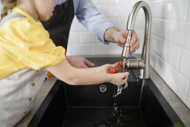 Tochter und Vater waschen Gemüse im Wasser, während sie in der Küche stehen - KMKF01530