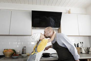 Daughter kissing father while standing in kitchen at home - KMKF01534