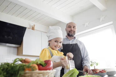 Daughter wearing apron preparing food while standing by father in kitchen at home - KMKF01537