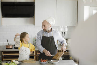 Girl showing grater to father while standing in kitchen at home - KMKF01550