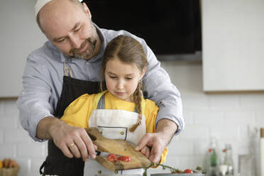 Father teaching daughter while standing in kitchen at home - KMKF01554