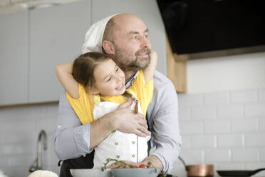 Father embracing daughter while standing in kitchen at home - KMKF01555