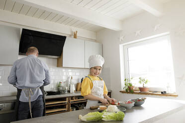 Lächelndes Mädchen beim Schneiden von Gemüse in der Küche zu Hause - KMKF01558