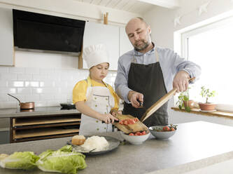 Tochter und Vater bereiten Essen zu, während sie zusammen in der Küche zu Hause stehen - KMKF01559