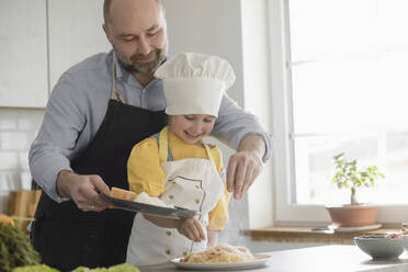 Lächelnder Vater und Tochter fügen Gewürze hinzu, während sie in der Küche zu Hause stehen - KMKF01562