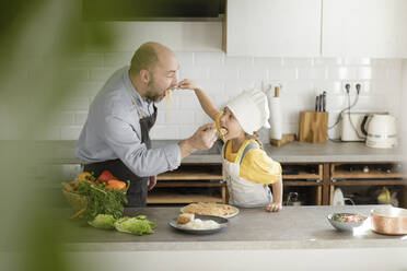 Vater und Tochter füttern sich gegenseitig mit Nudeln, während sie in der Küche zu Hause stehen - KMKF01568