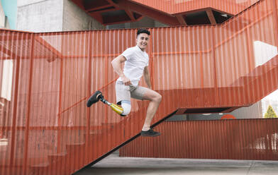 Young disabled man jumping against orange staircase - JCCMF01267