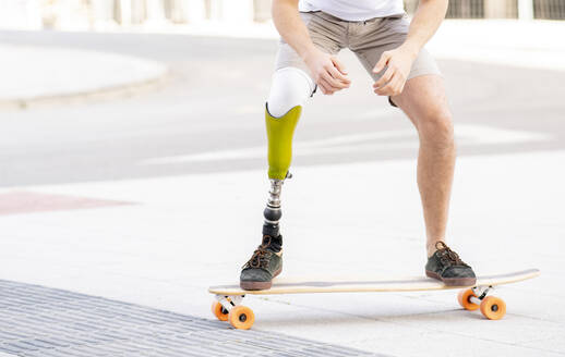 Junger Mann mit Behinderung fährt auf der Straße Skateboard - JCCMF01277