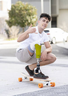 Smiling disabled man showing shaka sign while skateboarding on street - JCCMF01280
