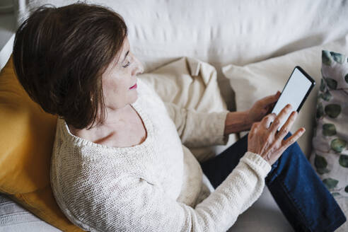 Ältere Frau benutzt ein Mobiltelefon, während sie zu Hause auf dem Sofa sitzt - EBBF02561