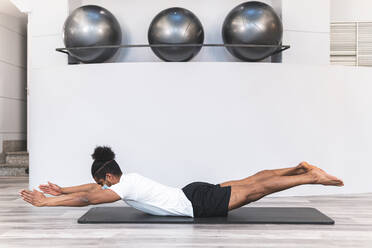 Mann übt Pilates auf einer Matte an der Wand im Yogastudio während COVID-19 - JAQF00304