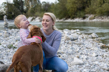 Young mother with her son and dog playing on riverbank - LBF03411