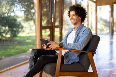 Lächelnder Mann, der ein digitales Tablet benutzt, während er im Vorgarten sitzt - SBOF02731