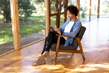 Man using digital tablet while sitting on armchair at front yard - SBOF02733