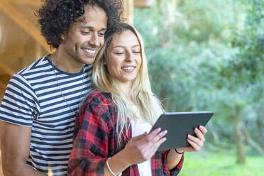 Junges Paar benutzt ein digitales Tablet, während es am Fenster im Vorgarten steht - SBOF02787