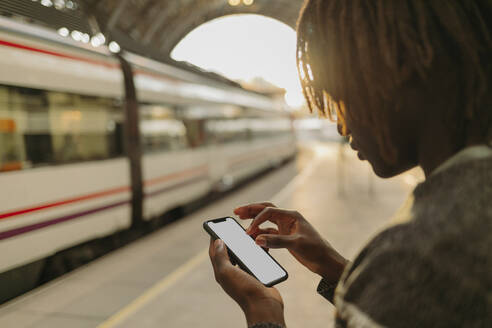 Young man using smart phone while waiting at railroad station - GMCF00015