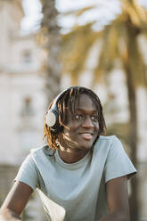 Young man listening music through headphones while looking away - GMCF00018