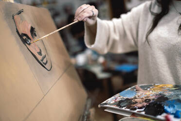 Weibliche Künstlerin malt Gesicht auf Leinwand in einem Kunststudio - JCCMF01295