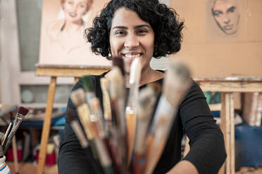 Lächelnde junge Malerin mit Pinseln im Kunstatelier - JCCMF01311