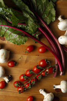 Rote Kirschtomaten mit essbaren Pilzen und Mangold auf Holztisch - IFRF00415