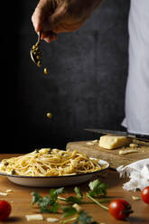 Mann gibt Kapern auf Spaghetti am Holztisch - IFRF00420