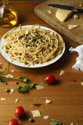 Plate of fresh spaghetti with capers amidst cilantro and cherry tomatoes on table - IFRF00422