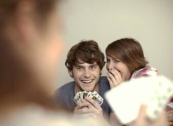 Frau flüstert einem jungen Mann ins Ohr, während er mit einem Freund zu Hause Karten spielt - AJOF01135