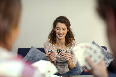 Beautiful woman smiling while playing cards with friends - AJOF01141