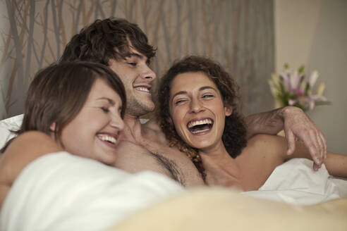 Lächelnder Mann liegt mit Frauen im Bett zu Hause - AJOF01144
