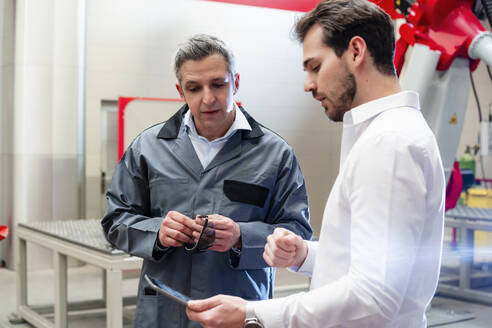 Männlicher Ingenieur, der ein digitales Tablet benutzt, während er mit einem Arbeiter in einer Fabrik diskutiert - DIGF14530