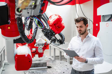 Junger Mann, der ein digitales Tablet mit einem Roboter in einer Fabrik benutzt - DIGF14538