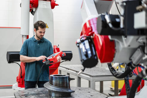 Männlicher Ingenieur, der einen Roboter über eine Steuerung bedient, während er in einer Fabrik steht - DIGF14564