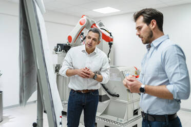 Male entrepreneurs looking at white board while standing in factory - DIGF14593