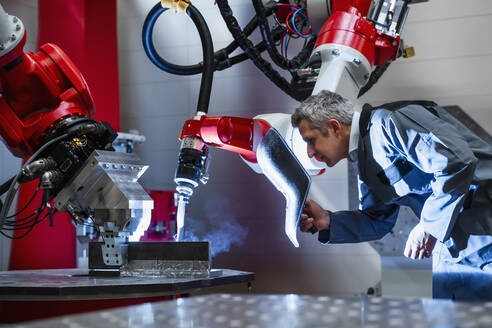 Älterer Arbeiter mit Schweißhelm bei der Arbeit an einem Roboter in einer Fabrik - DIGF14596