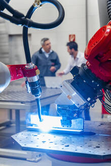 Roboterschweißbrenner schweißt, während männliche Unternehmer in der Fabrik arbeiten - DIGF14614