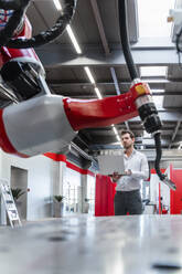 Roboter-Schweißbrenner, während ein junger Mann in einer Fabrik mit einem Laptop arbeitet - DIGF14621