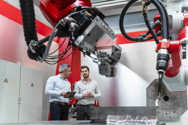 Male automation engineers discussing while robotic machinery in foreground - DIGF14627