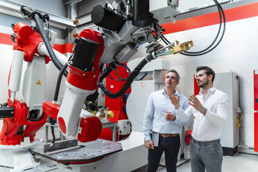 Male engineers discussing over robotic machinery in factory - DIGF14628