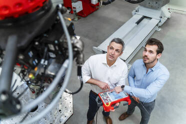 Männliche Ingenieure bei der Bedienung von Robotern mit Steuerung in einer Fabrik - DIGF14649