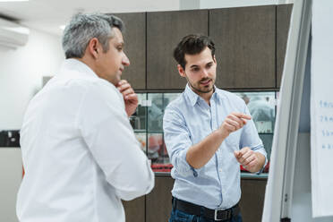 Young male entrepreneur discussing plans with colleague at whiteboard - DIGF14676