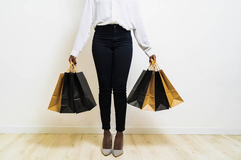 Junge Frau trägt Papier-Einkaufstaschen, während sie vor einem weißen Hintergrund steht - GIOF11372