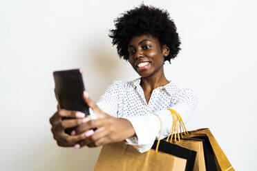 Lächelnde Frau, die ein Selfie mit ihrem Mobiltelefon macht, während sie vor einem weißen Hintergrund steht - GIOF11373