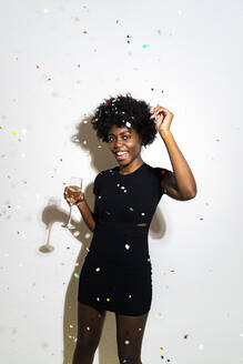 Konfetti fällt auf glückliche Frau tanzen mit Champagner-Flöte, während stehend gegen weißen Hintergrund - GIOF11387
