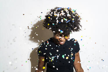 Smiling woman with confetti falling on head standing against white background - GIOF11391