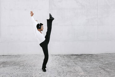 Flexible male dancer stretching leg while practicing urban dance against white wall - TCEF01580