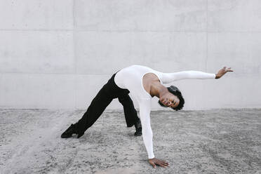 Flexible man bending over backwards while dancing against white wall - TCEF01581