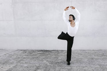 Male dancer balancing on one leg while dancing in white wall - TCEF01582