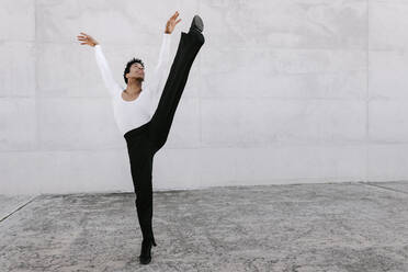 Flexible male dancer looking up while stretching leg against wall - TCEF01594