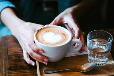 Anonyme Frau hält eine Tasse mit frischem, heißem, aromatischem Kaffee und ein Glas Wasser in einem Café - ADSF20988